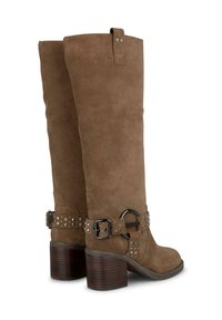 Botas de ante marrón hasta la rodilla con un tacón grueso, que cuentan con un cinturón ancho con tachuelas y un anillo metálico sobredimensionado. Textura suave, construcción robusta.
