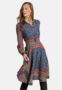 Vestido de satén en azul con patrones circulares y rayados en rojo y verde. Presenta un cuello y mangas largas, con botones en la parte delantera.