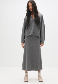 Haut en tricot gris à col en V et épaules tombantes, assorti d'une jupe maxi grise. Présente une texture douce et une coupe décontractée.