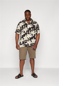 Camisa negra de manga corta con patrón floral blanco, combinada con pantalones cortos beige y sandalias negras tipo slides. Diseño simple y ajuste relajado.