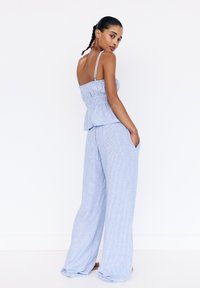 Lichtblauwe gestreepte twee-delige outfit met een smocked lijfje en breed uitgesneden broek. Zachte stof met verstelbare bandjes en zijzakken.