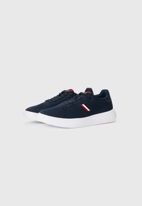 Navy blue fabric sneakers with white rubber soles, featuring round laces and a tri-color accent near the ankle in red, white, and blue.