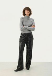 Grauer Rollkragenpullover kombiniert mit schwarzen, mit Pailletten besetzten, weiten Hosen. Das Material wirkt weich, die glänzenden Pailletten erzeugen eine strukturierte Oberfläche.