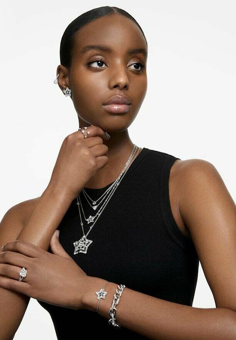 Silberne Schmuckstücke mit geschichteten Ketten, sternförmigen Anhängern und Ringen. Ein Armband mit Sternakzenten und glatten Oberflächen. Modell trägt ein schwarzes Oberteil.