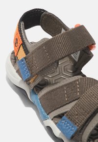 Brun tygsandall med justerbara remmar, med orange och blå accentfärger, texturerad sula och gummibotten för grep.