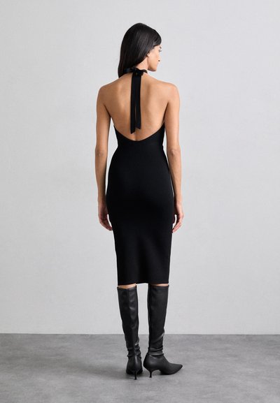 Mustmust musträtik, millel ei ole varrukasid, madala seljaosa ja kaela sidumisvõimalusega. Rätt on selga sobiv ja ulatub keskmise sääre kõrgusele. Kombineeritud mustade kõrge kontsaga saapadega, mis ulatuvad põlvini.