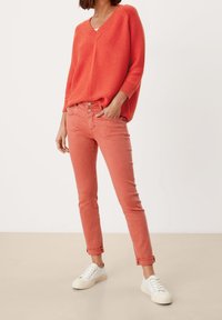 Maglione corallo a coste con scollo a V, abbinato a jeans aderenti color corallo chiaro. Sneakers bianche completano il look.