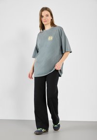 Oversized, light gray cotton t-shirt featuring a yellow sun graphic, paired with black wide-leg pants and blue shoes with green accents.