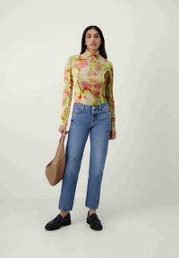 Top de manga larga con estampado floral en colores pastel, combinado con jeans de pierna recta de lavado claro. La modelo sostiene un bolso color beige y lleva unos loafers oscuros.