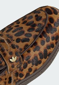 Παπούτσια slip-on με λεοπάρ σχέδιο, με υφή γούνινης επιφάνειας, καφέ λεπτομέρειες και χρυσό διακοσμητικό λογότυπο στο λουράκι.