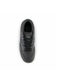 Chaussure de sport noire avec un dessus en cuir lisse, accents gris, six œillets et col rembourré. Présente le logo "newbalance" sur la languette.