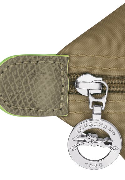 Tan nylon bag with a textured leather accent, featuring a silver zip pull adorned with a circular logo and a green trim around the edge.