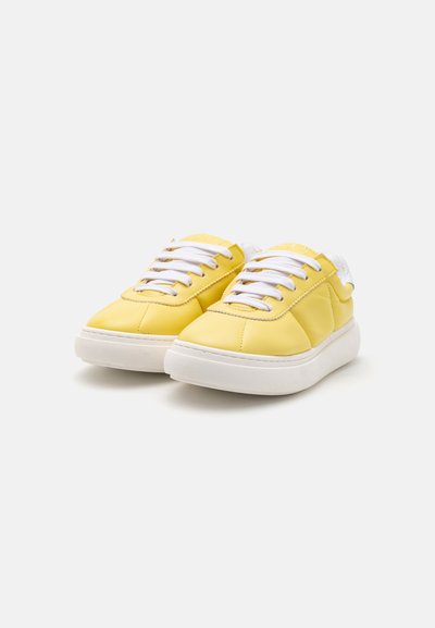 Gula lädersneakers med en slät yta, vita snören och en tjock vit gummisula. Har en minimalistisk design och rund form.