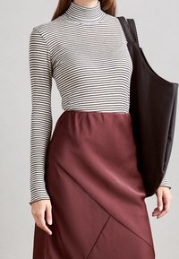 Mustat ja valkoiset raidalliset poolopaita yhdistettynä burgundinväriseen hameeseen, jossa on vinosaumoja. Musta laukku roikkuu yhdellä olalla.