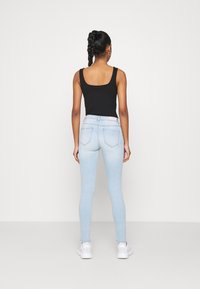 Top negro sin mangas combinado con jeans ajustados azul claro, con cintura alta y bolsillos traseros, sobre un fondo blanco.