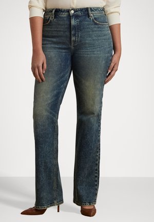 Personne portant un jean bleu délavé taille haute et jambes droites, avec des talons pointus marron et une chemise à manches longues de couleur claire.