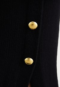 Close-up of black ribbed fabric with two gold round buttons embossed with "Barbour International" text.