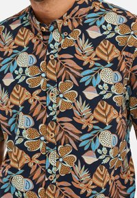 Korte mouwen shirt van donkerblauwe stof met kleurrijke bloem- en bladerenpatronen in oranje, groen en lichtblauw, met knoopsluiting.