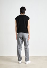 Svart ärmlös topp och ljusgrå byxor. Slät tyg, enkel design, med platta sömmar. Vita sneakers kompletterar outfiten.