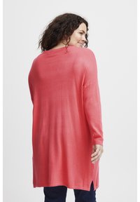 Maglione a maniche lunghe in maglia corallo con un fit rilassato, spacchi laterali e polsini a costine. La texture sembra morbida e leggera.