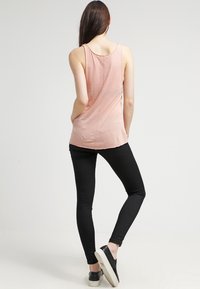 Ljusrosa ärmlös topp med lös passform, matchad med svarta leggings och svarta slip-on skor, visad bakifrån.