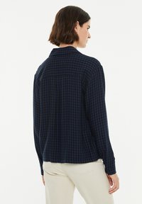 Camisa de cuadros en azul marino de material de franela, con cuello, puños de botón y detalle en la yugo trasero. Mangas largas, corte relajado.