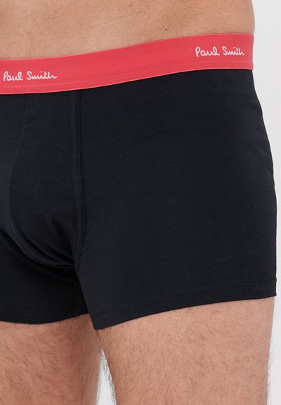 Boxers noirs avec une ceinture élastique rouge comportant "Paul Smith" en texte blanc. Le tissu semble lisse avec un design ajusté.