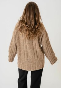 Svijetlosmeđi pleteni pulover s rebrastom teksturom, širokog kroja i širokim rukavima. Kratki rub straga, bez vidljivih zatvarača ili uzoraka.