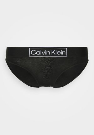 Zwarte katoenen slip met een brede elastische tailleband met daarop een wit "Calvin Klein" logo. Gladde textuur en klassieke slip snit.