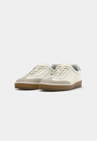 Sneakers met een beige en witte uitstraling, gemaakt van suède en leer, met een ronde neus, een lichte gumzool en textuuraccenten.