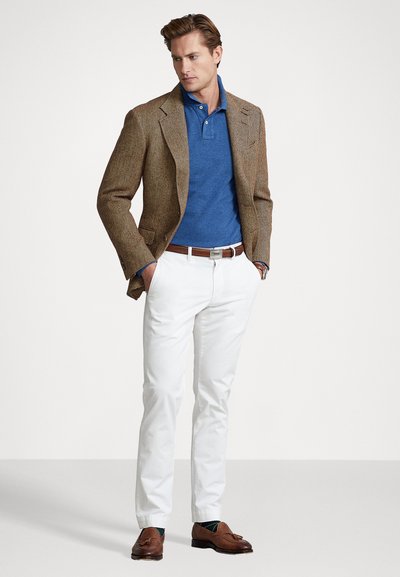 Ruskea herringbone-bleiseri sinisen poolopaidan päällä, valkoiset housut ja ruskeat loaferit. Asusteeseen kuuluu ruskea vyö ja teksturoitu kangas.