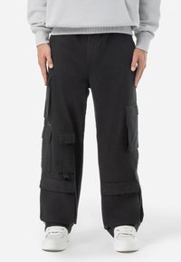 Black cargo pants made of cotton, featuring multiple pockets, a relaxed fit, and cuffed hems, paired with white sneakers.