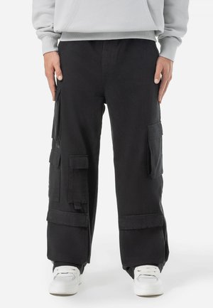 Svarta cargobyxor i bomull, med flera fickor, avslappnad passform och uppvikta benslut, kombinerat med vita sneakers.