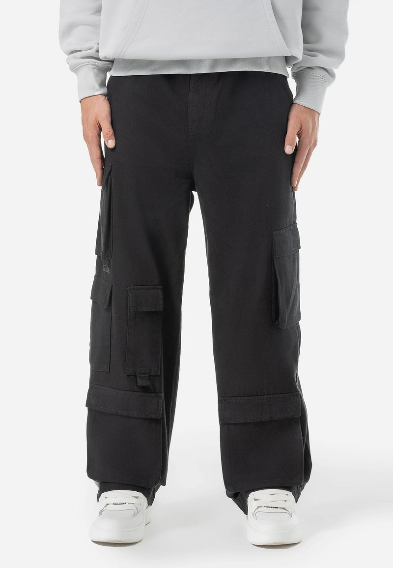 Black cargo pants made of cotton, featuring multiple pockets, a relaxed fit, and cuffed hems, paired with white sneakers.
