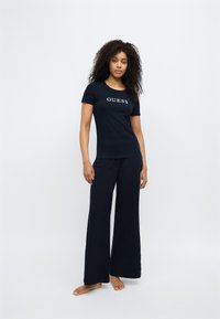 Marineblauw set bestaande uit een T-shirt met korte mouwen en "GUESS" logo en een broek met wijde pijpen. Gladde stof met een losse pasvorm, geschikt als comfortabele loungewear.