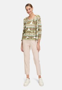Green and beige patterned top with three-quarter sleeves, paired with light beige tapered pants and white sneakers.