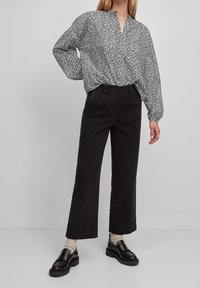 Zwart-witte blouse met een V-hals en ballonmouwen, gecombineerd met hoge zwarte broeken en stevige zwarte instappers.