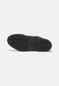 Semelle de botte en caoutchouc noir avec un motif de semelle profond, arborant un logo et un talon renforcé pour une meilleure adhérence et durabilité.