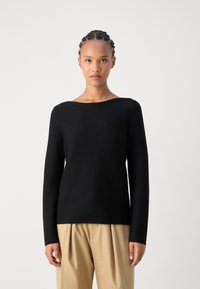Schwarzer Pullover mit langen Ärmeln und weitem Ausschnitt, aus strukturiertem Strickstoff und mit lässiger Passform, kombiniert mit beigen, plissierten Hosen.