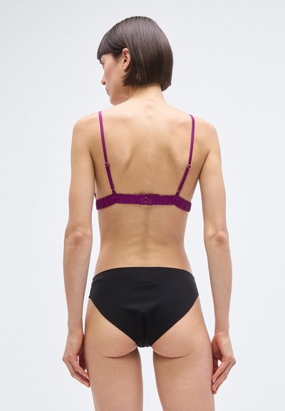 Fioletowy biustonosz z cienkimi ramiączkami i marszczoną opaską, w zestawieniu z czarnymi majtkami bikini. Gładka faktura, minimalistyczny design i niska talia.