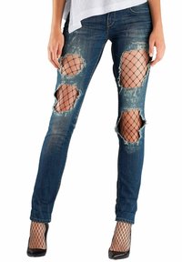 Jeans en denim bleu déchiré avec de grandes zones trouées révélant un filet noir en dessous. Design ajusté avec un léger stretch et une teinte foncée.
