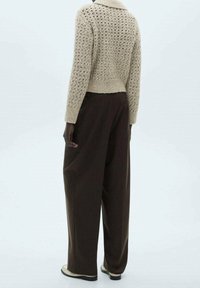 Beżowy sweter dzianinowy o luźnym kroju i kołnierzu, połączony z brązowymi spodniami o szerokich nogawkach oraz beżowymi butami z czarną podeszwą.