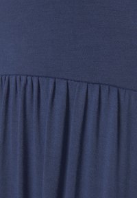 Ύφασμα σε ναυτικό μπλε με λεία υφή, που διαθέτει μια επίπεδη περιοχή στο επάνω μέρος και πιέτες στο κάτω μέρος για επιπλέον διάσταση και οπτικό ενδιαφέρον.