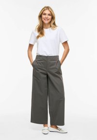 Balti medvilniniai marškinėliai, derinami su aukštu liemeniu ir plačiomis pilkomis kelnėmis. Batai balti su apskritais akcentais. Viskas pasižymi lygia tekstūra.