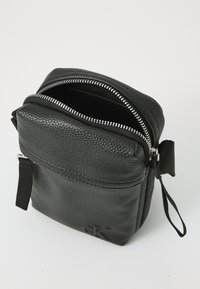 Black leather bag with a textured surface, zippered top, and front pocket. Features silver zipper hardware and an attached fabric loop.