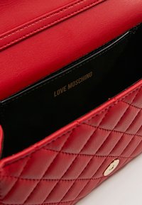Vnitřek červené prošívané kožené kabelky, s černou podšívkou a zlatým logem "LOVE MOSCHINO". Viditelné magnetické zapínání.