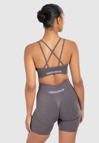 Grijze sportbeha met kruisende banden gecombineerd met high-waisted shorts, beide met het "SMILODOX"-logo in het wit op de tailleband.