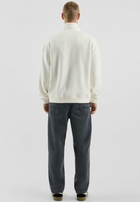Biała bluza z długim rękawem i wysokim kołnierzem, w połączeniu z ciemnoszarymi, luźnymi jeansami z dwoma tylnymi kieszeniami i subtelnymi detalami szwów.