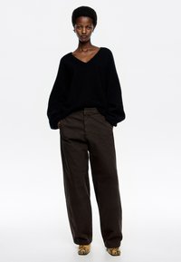 Suéter negro de punto oversized con escote en V, combinado con pantalones de pierna ancha marrón oscuro. Presenta una tela texturizada y tacones con estampado de serpiente.