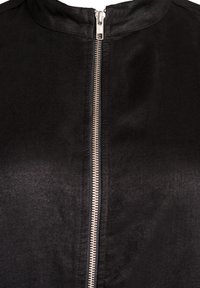 Schwarze Jacke mit hohem Kragen, ausgestattet mit einem Frontreißverschluss und einer glatten, weichen Textur. Der Reißverschluss ist silberfarben und verläuft mittig.
